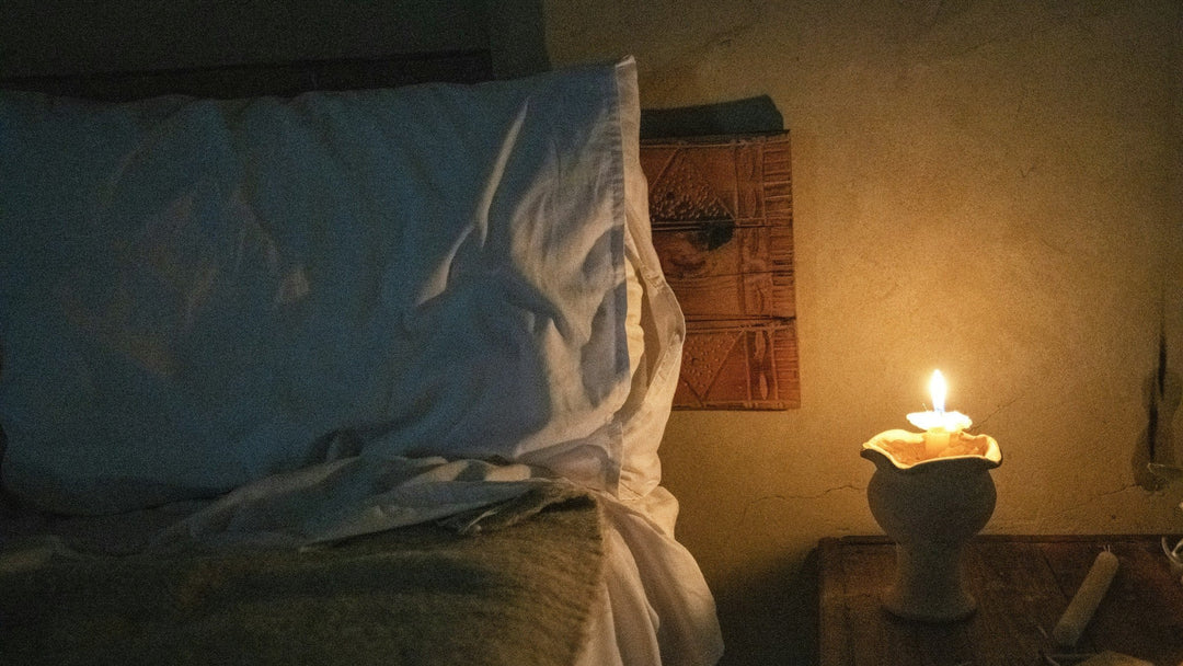 A candle glowing in a ceramic holder beside a white linen pillow at night