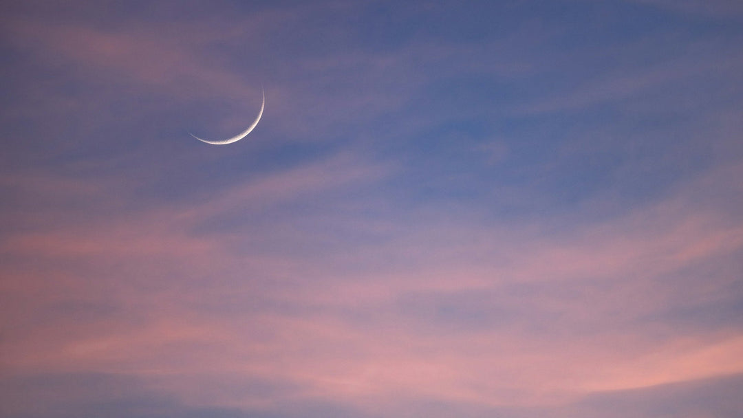 A crescent moon in a soft pink and lavender twilight sky